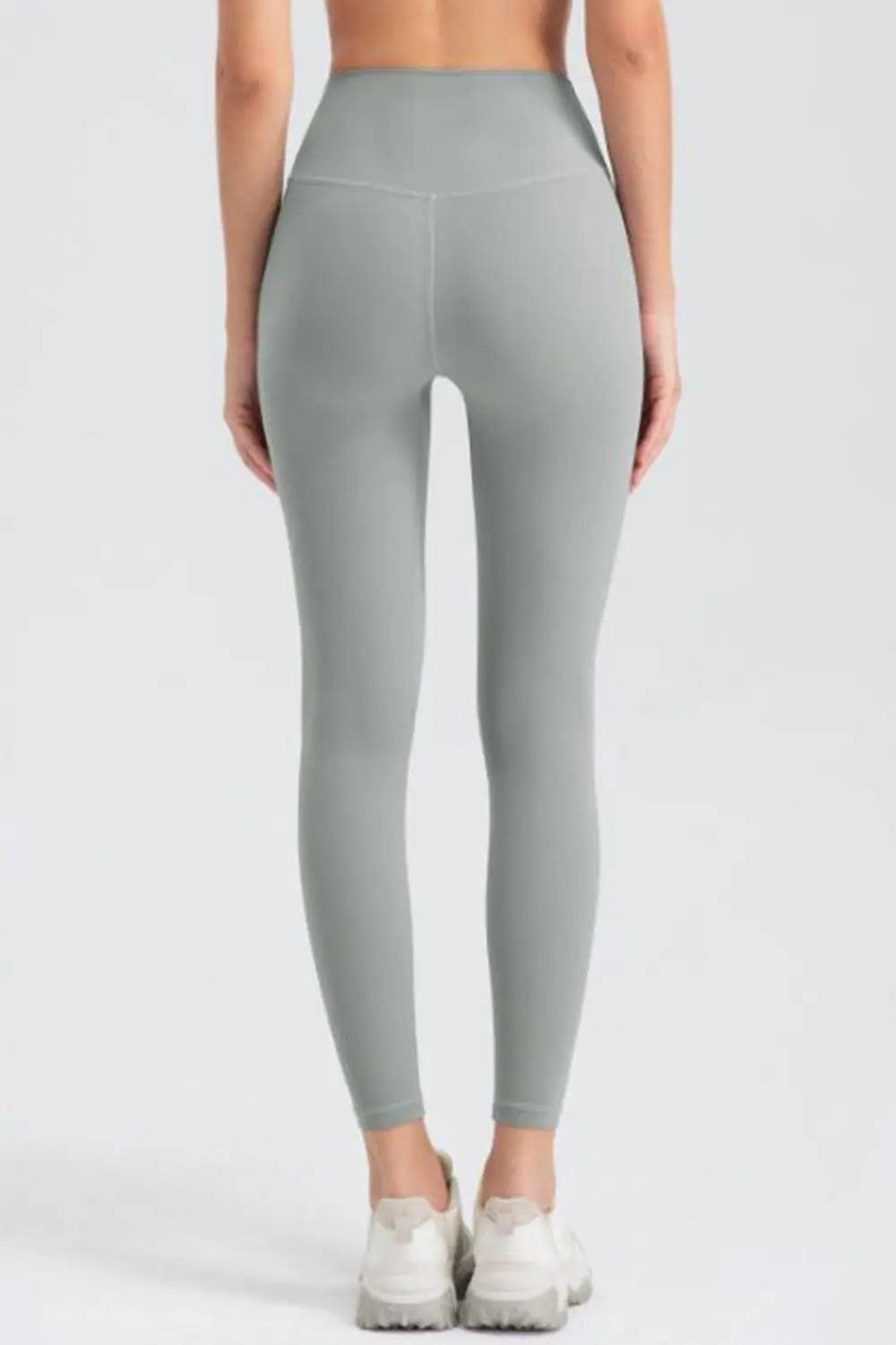 Model stands facing away in gray wide-waistband slim-fit active leggings with a high-rise silhouette, smooth construction, and ankle-length tapered legs.