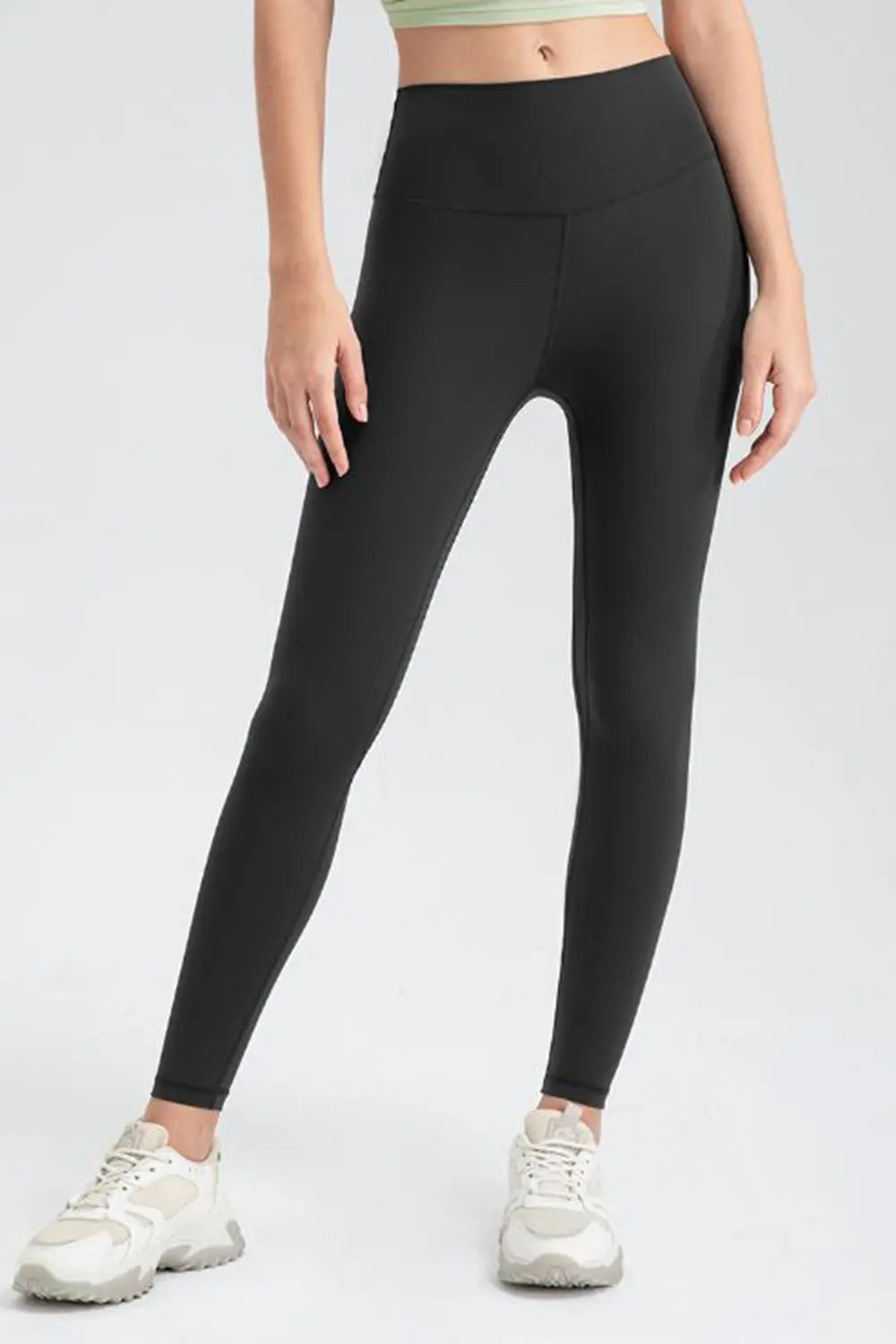 Model stands with legs apart in black slim-fit active leggings featuring a wide waistband, smooth stretch construction, and full-length tapered legs.