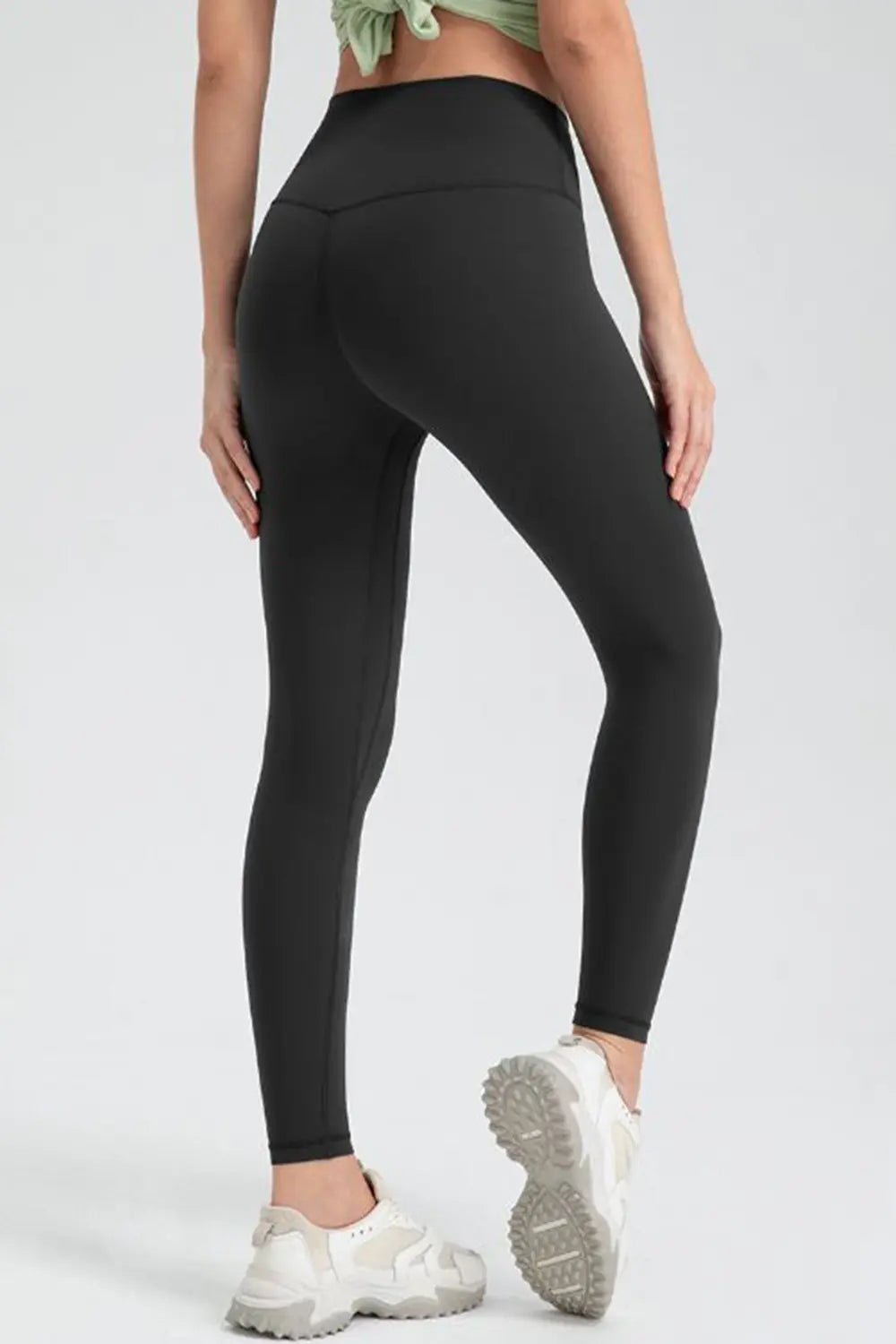 Model poses in black slim-fit active leggings with a wide waistband, smooth stretch construction, and ankle-length silhouette.