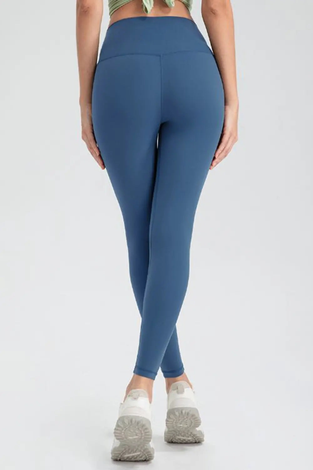 Model shown from behind in blue slim-fit active leggings with a wide waistband, smooth stretch construction, and ankle-length silhouette.