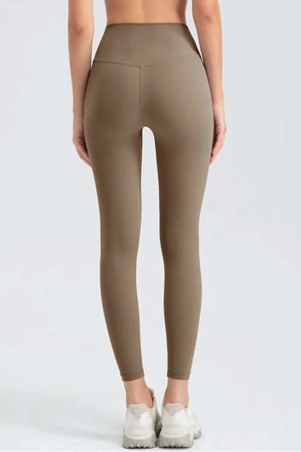 Model shown from behind wearing taupe slim-fit active leggings with a wide waistband, ankle-length silhouette, and visible center-back seam.