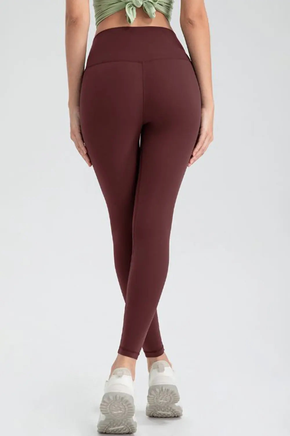 Model stands with legs crossed, wearing burgundy wide waistband slim fit active leggings with a smooth, stretchy ankle-length silhouette.