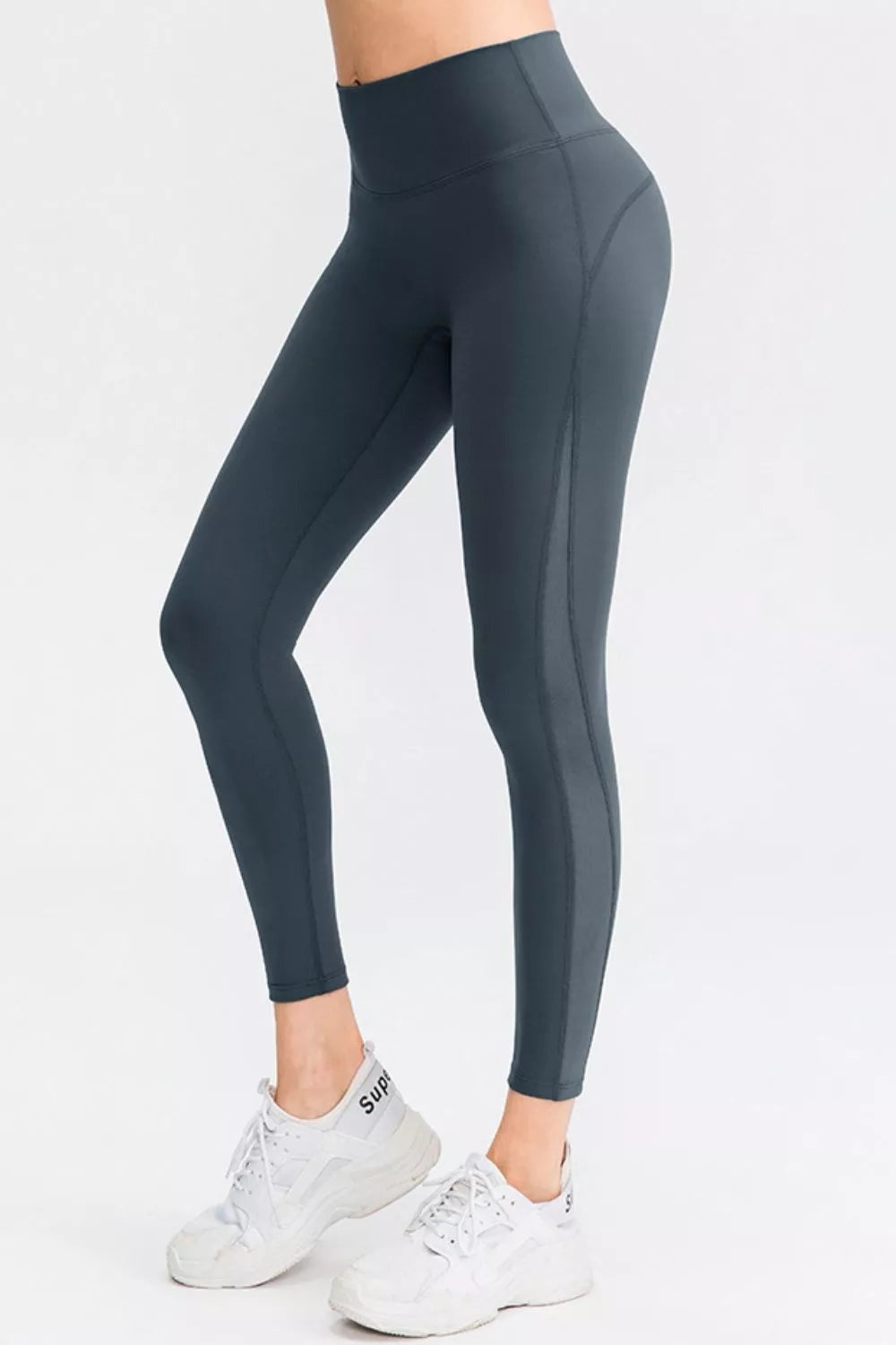 Model wearing solid charcoal slim-fit sports leggings with a wide waistband, long ankle-length silhouette, and visible seam construction, posing with one knee bent.
