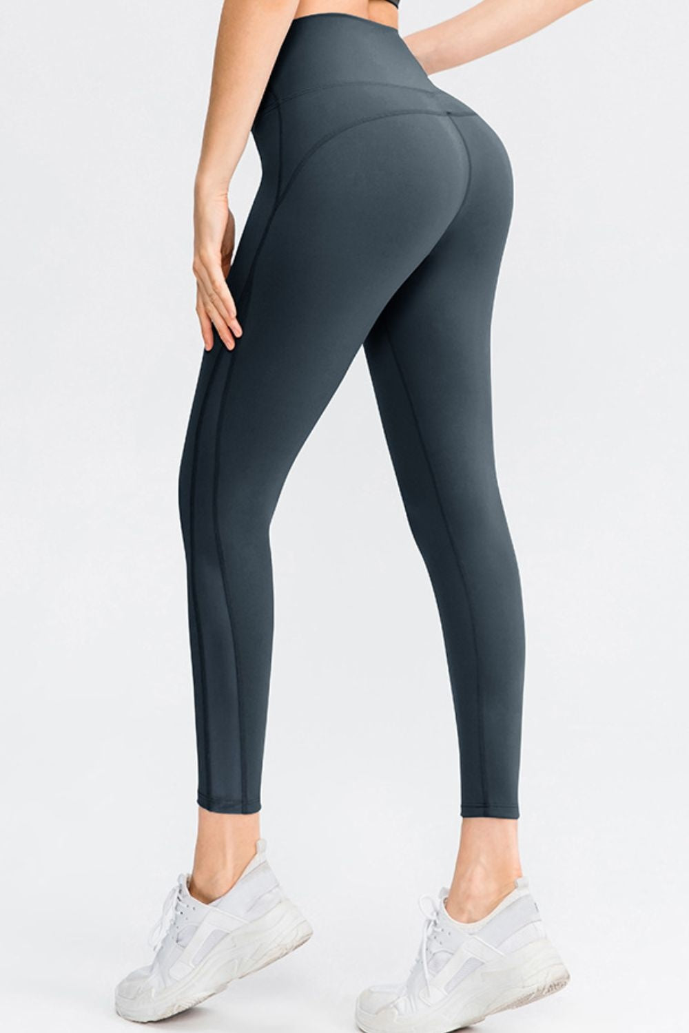 Model poses from the back in solid charcoal slim-fit long sports leggings with a wide waistband, contoured seams, and tapered ankle-length legs.