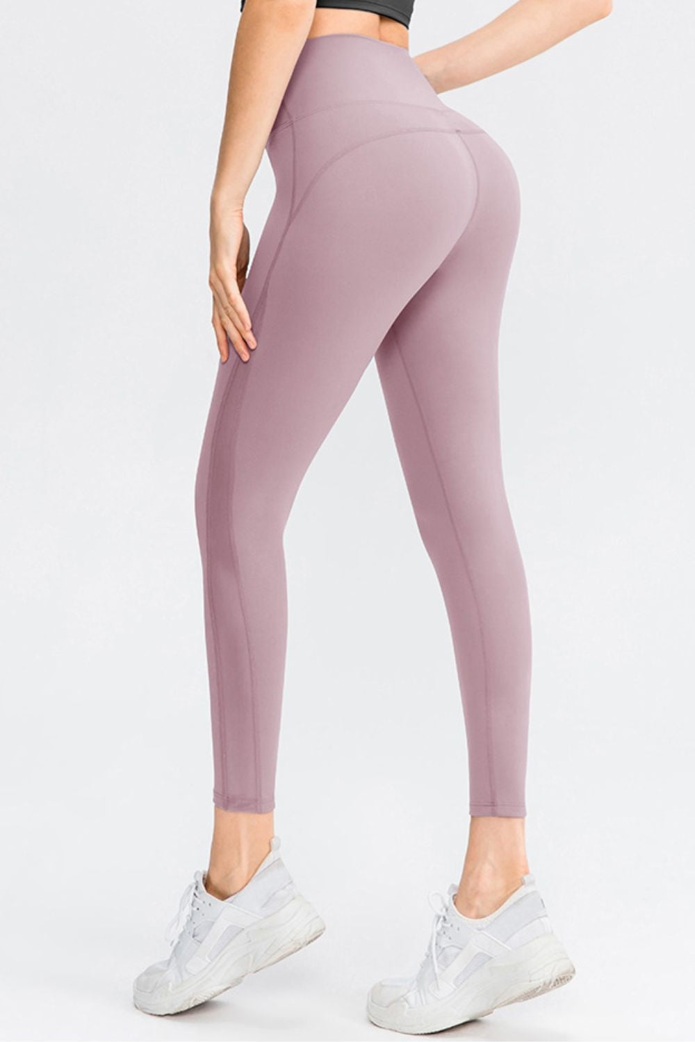Model wearing mauve solid long sports leggings with a wide waistband, slim-fit silhouette, and visible curved seam construction, posed from the back.