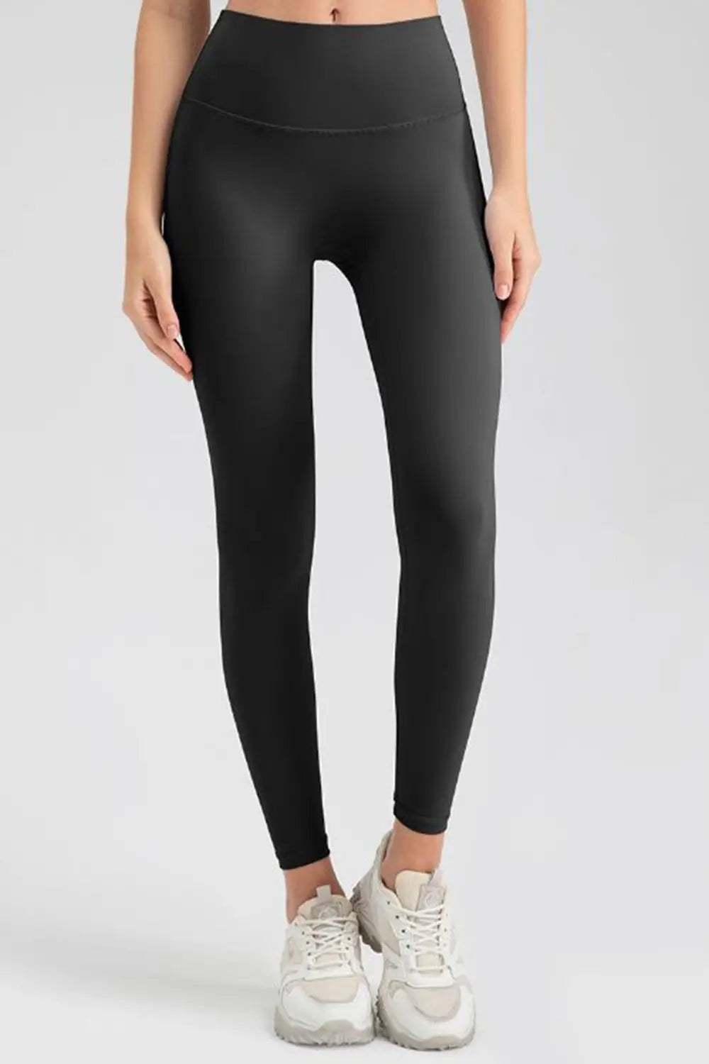 Model stands wearing black wide-waistband sport leggings with a high-rise fit, smooth construction, and slim full-length silhouette.