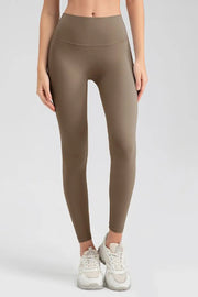 Model stands facing forward in brown wide waistband sport leggings with a sleek, stretchy, close-fitting silhouette and ankle-length hems.