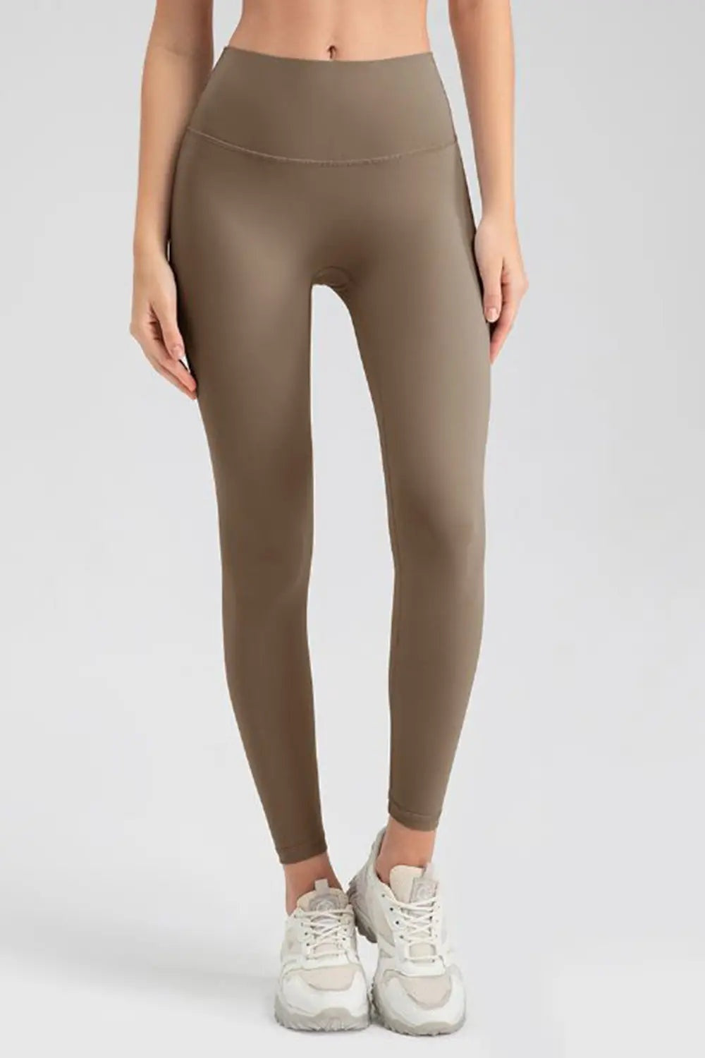 Model stands facing forward in brown wide waistband sport leggings with a sleek, stretchy, close-fitting silhouette and ankle-length hems.