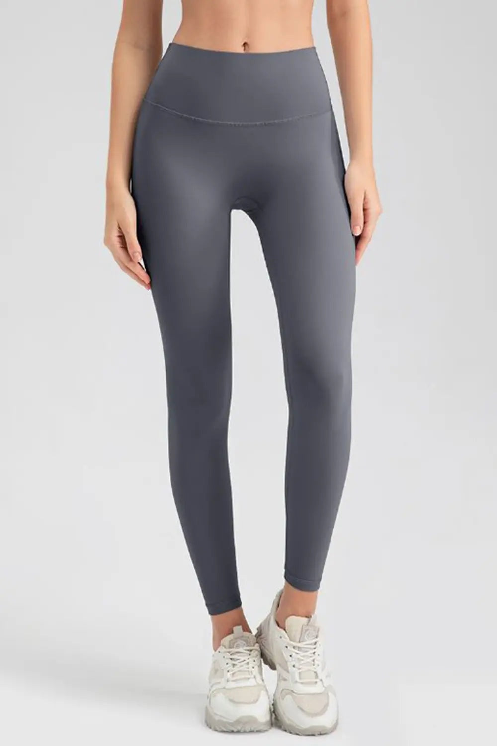 Model stands with hands at her sides wearing charcoal gray wide waistband sport leggings with a high-rise, fitted silhouette and ankle-length tapered legs.