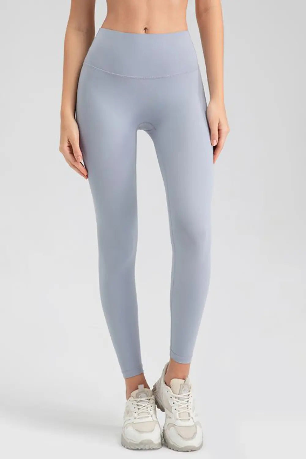 Model wearing light blue high-waisted sport leggings with a wide waistband, smooth construction, and slim ankle-length silhouette, standing with hands at her sides.