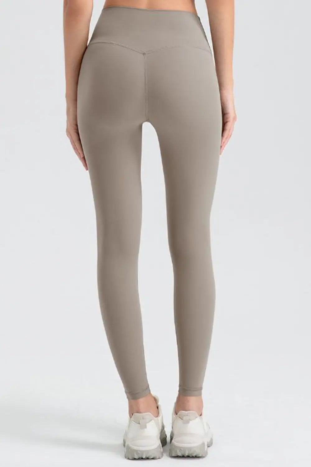 A rear view shows a model in taupe wide waistband sport leggings with a fitted full-length silhouette, smooth stretch fabric, and visible center seams.