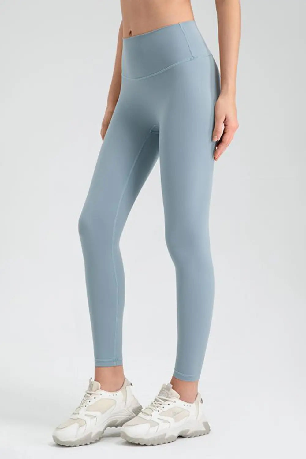 Model standing in light blue wide waistband sport leggings with a high-rise fit, ankle-length slim silhouette, and visible panel seams.