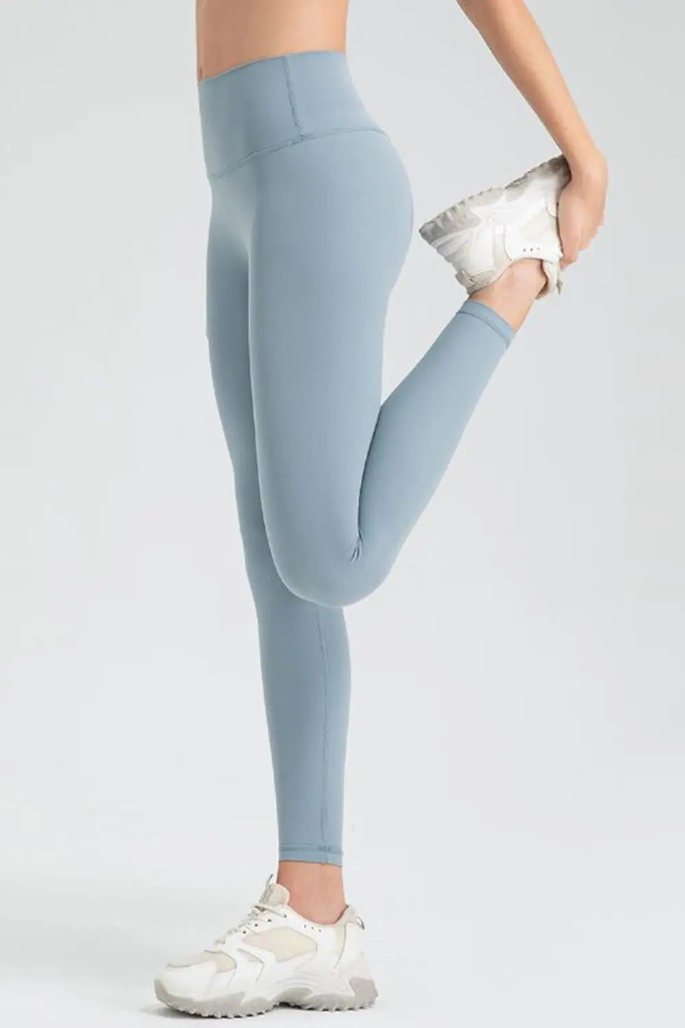 Model stretches in light blue wide-waistband sport leggings with a fitted full-length silhouette and smooth seamed construction.
