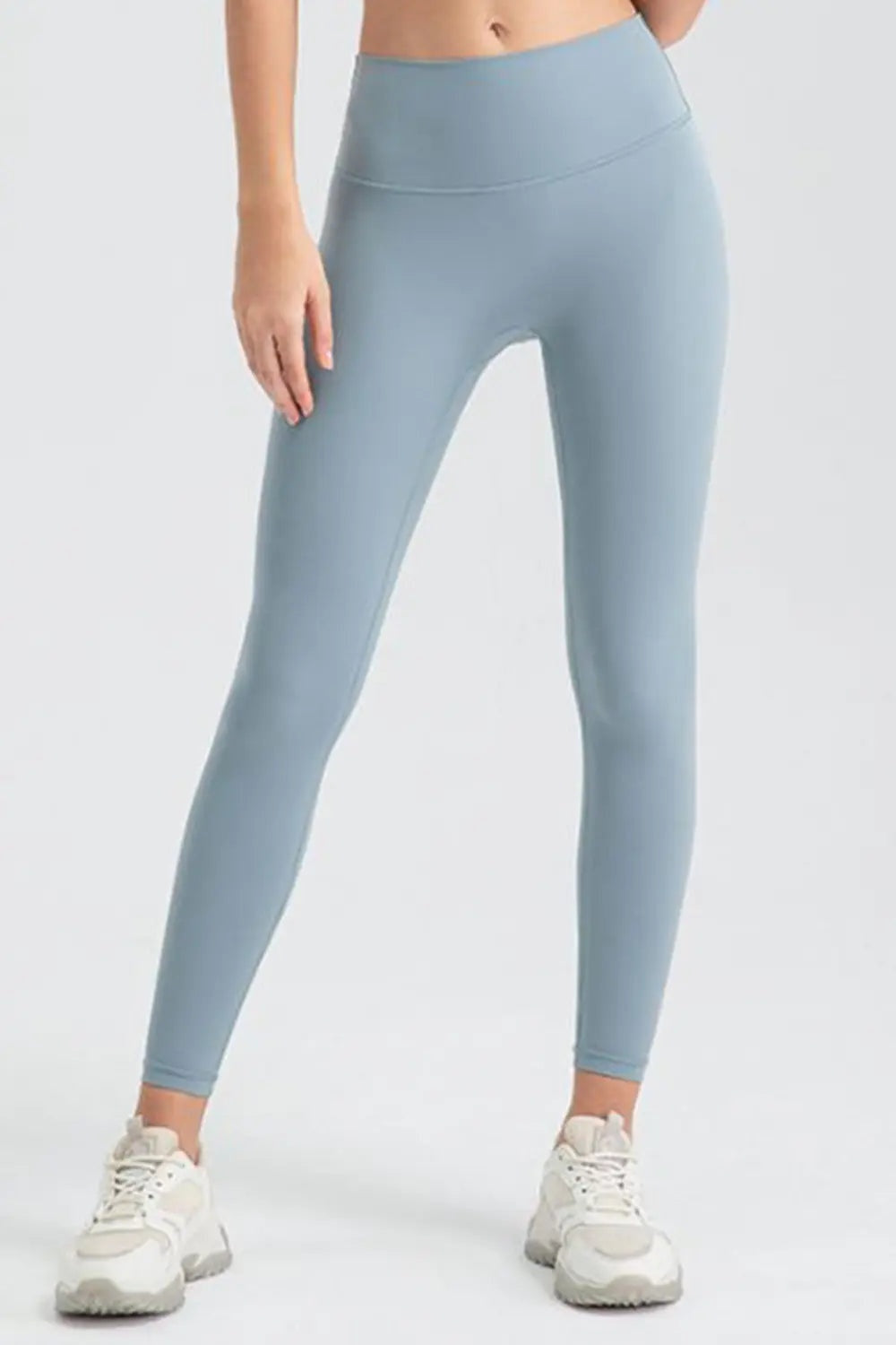 Model stands with legs apart wearing light blue sport leggings featuring a wide waistband, fitted full-length silhouette, and curved front seam construction.