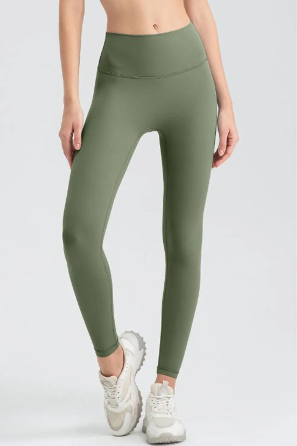 Model wearing olive green wide waistband sport leggings with a high-rise, fitted full-length silhouette and curved seam detail, standing with one leg crossed.