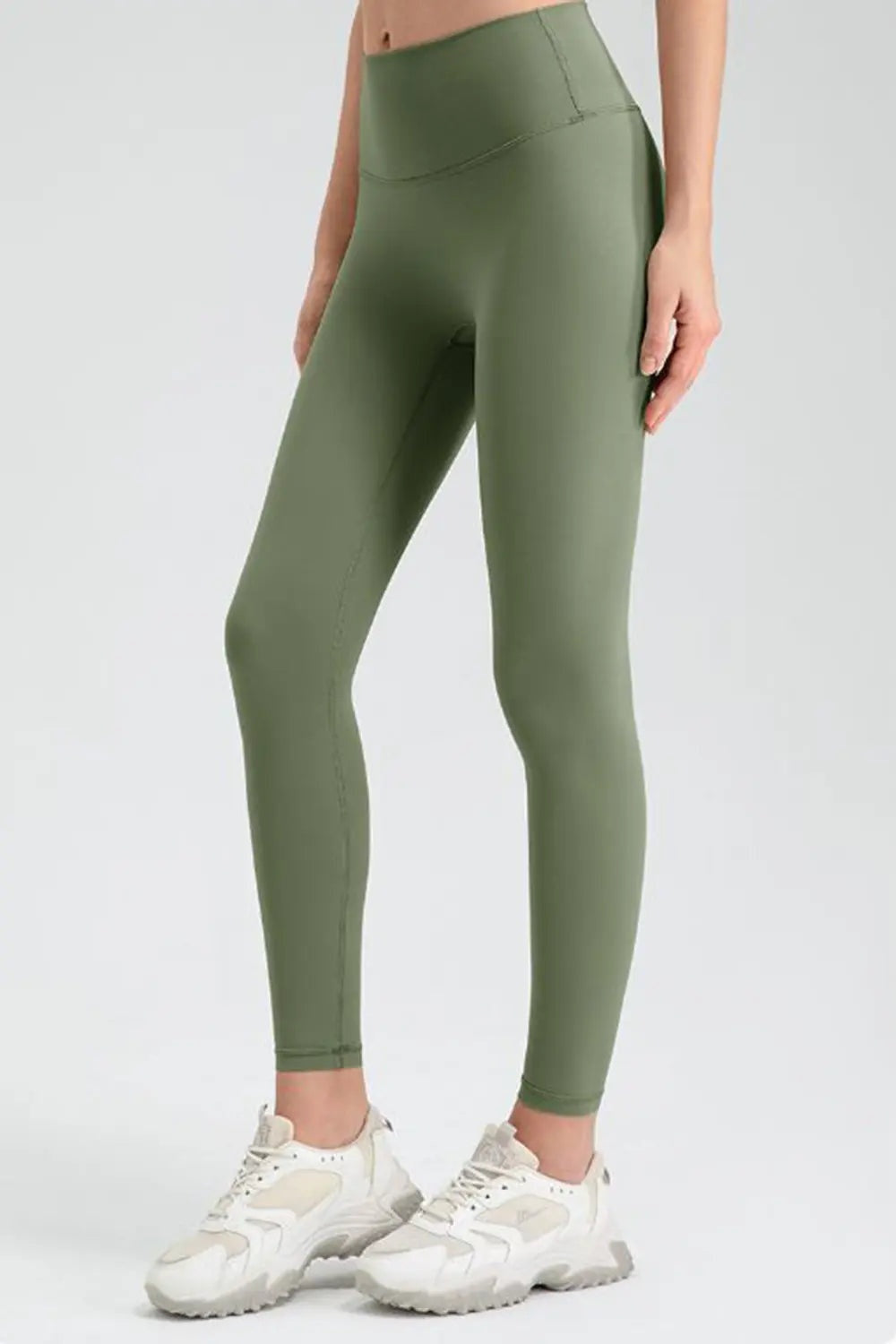 Model poses in olive green wide-waistband sport leggings with a high-rise fit, ankle-length tapered silhouette, and visible curved waistband seams.