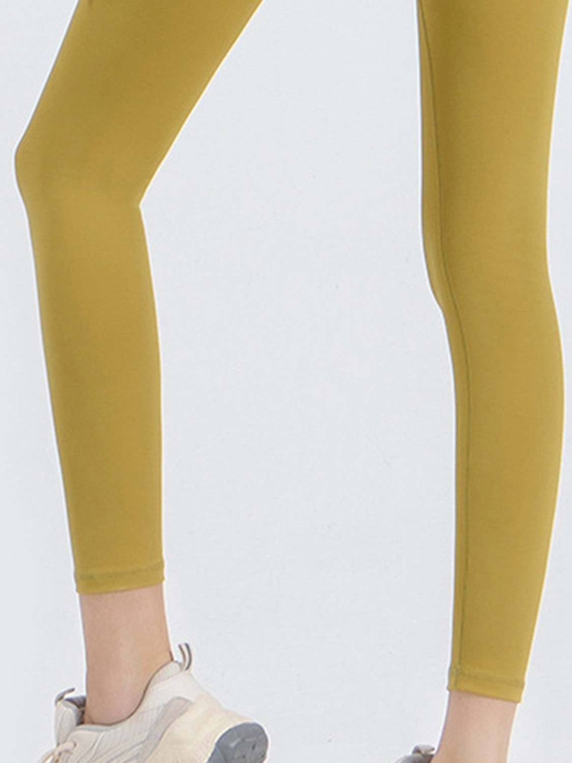 Model wears opaque mustard-yellow sports leggings with a close, stretchy full-length silhouette, shown on legs with one knee slightly bent.