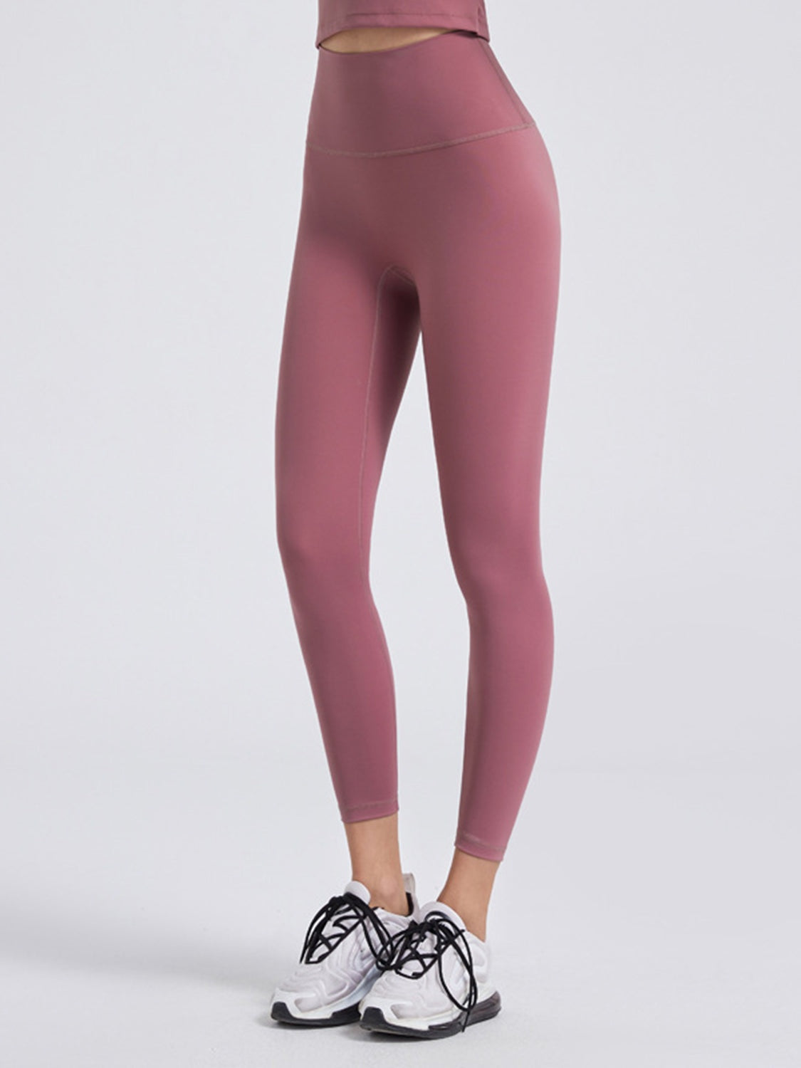 Model wears mauve wide waistband sports leggings with a high-rise silhouette, fitted full-length legs, visible seams, and a stretchy opaque construction.