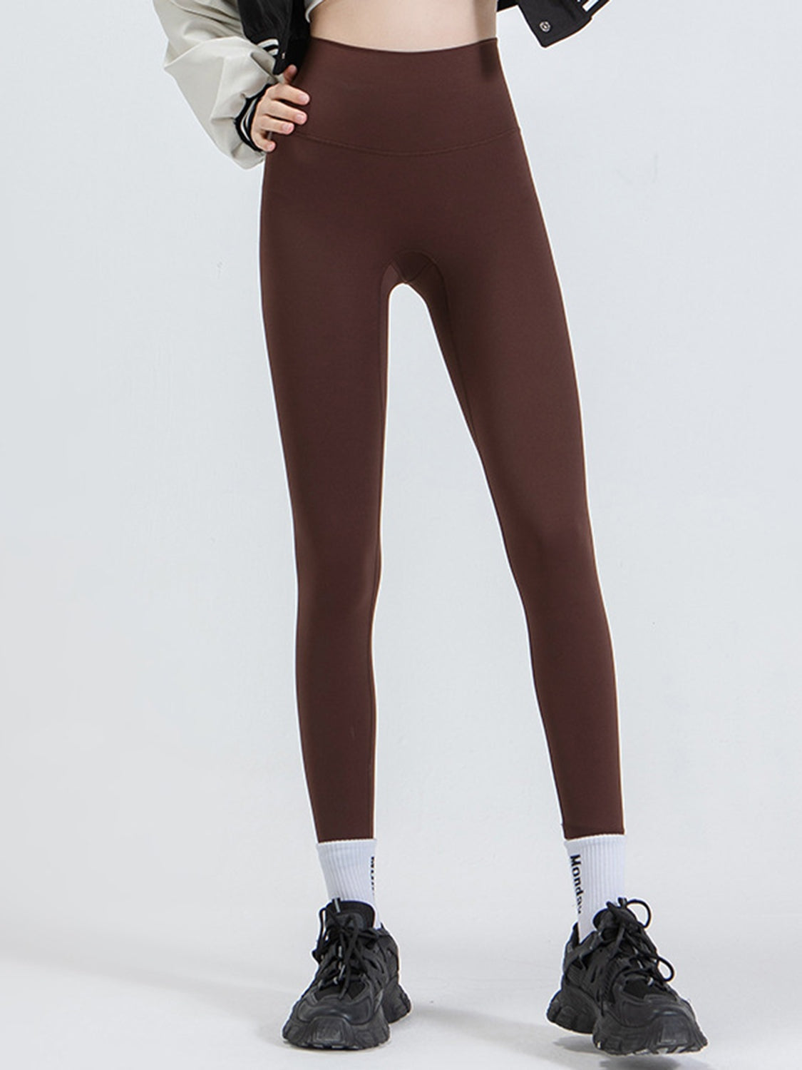 Model stands with one hand on her hip, wearing dark brown wide-waistband sports leggings with a high-rise fit and slim full-length silhouette.