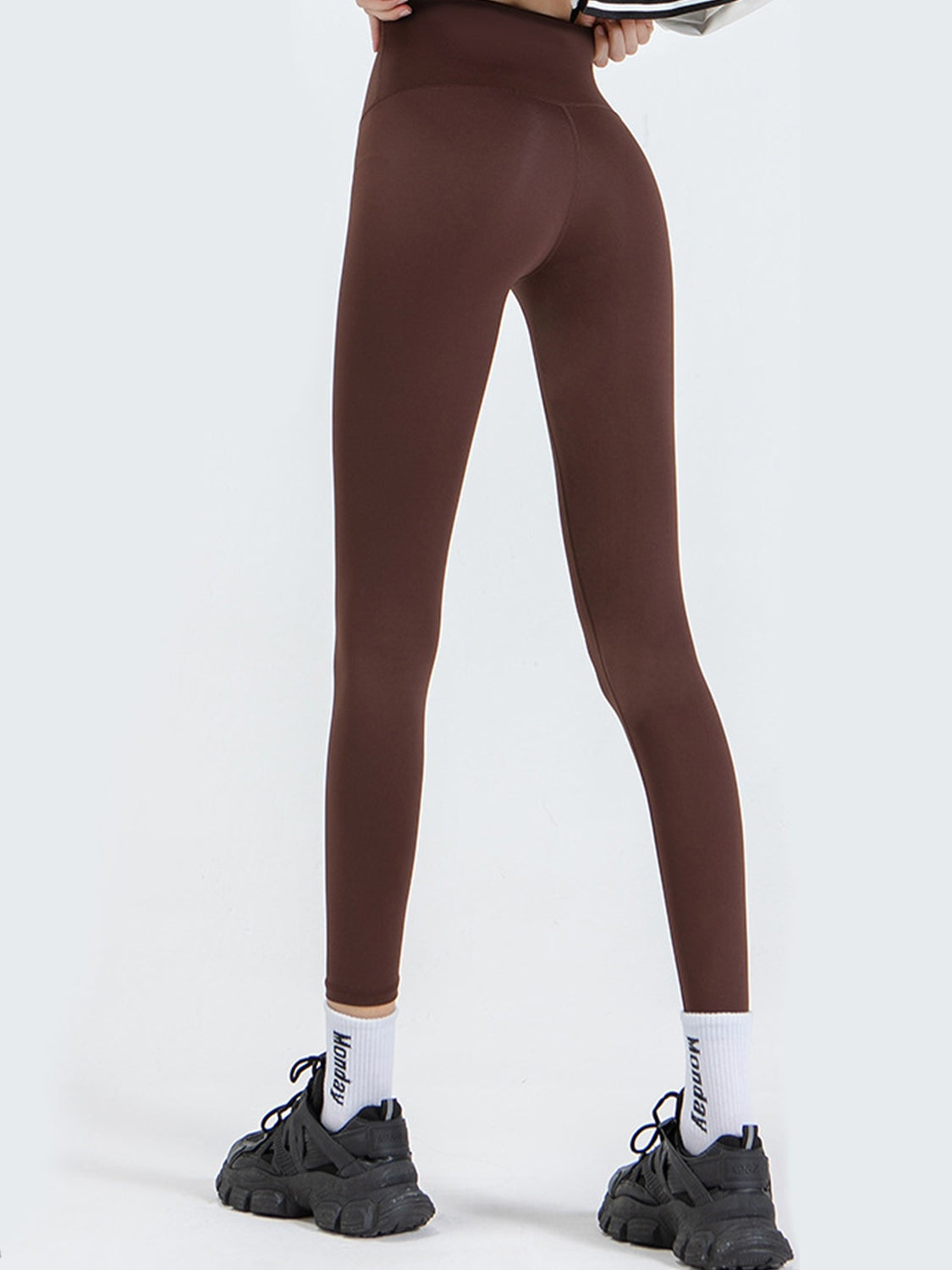 Model wearing brown wide waistband sports leggings with a high-rise fit, smooth opaque fabric, full-length slim silhouette, and subtle seams.