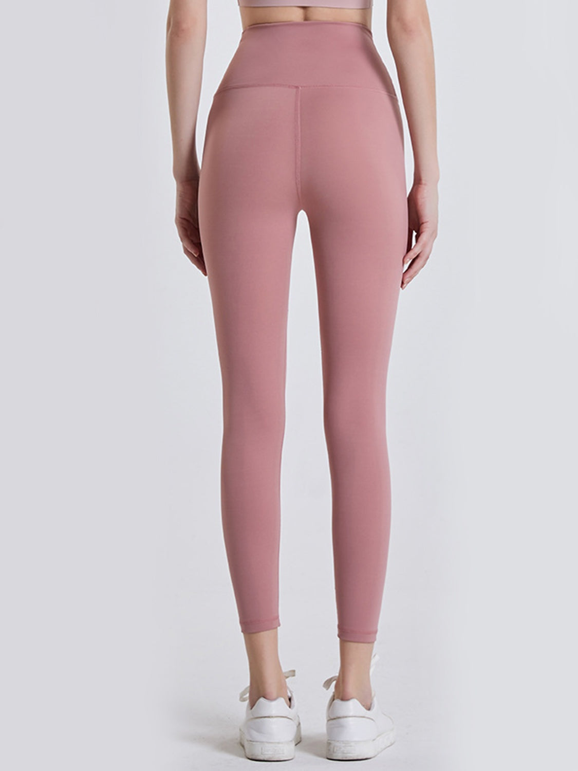 Model shown from behind wearing dusty pink wide waistband sports leggings with a high-rise fit, ankle-length tapered silhouette, and center-back seam.