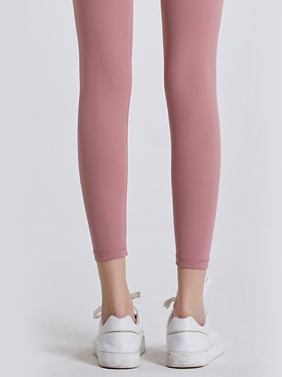 Model shown from behind wearing pink sports leggings with a close, stretchy ankle-length silhouette and clean hems.