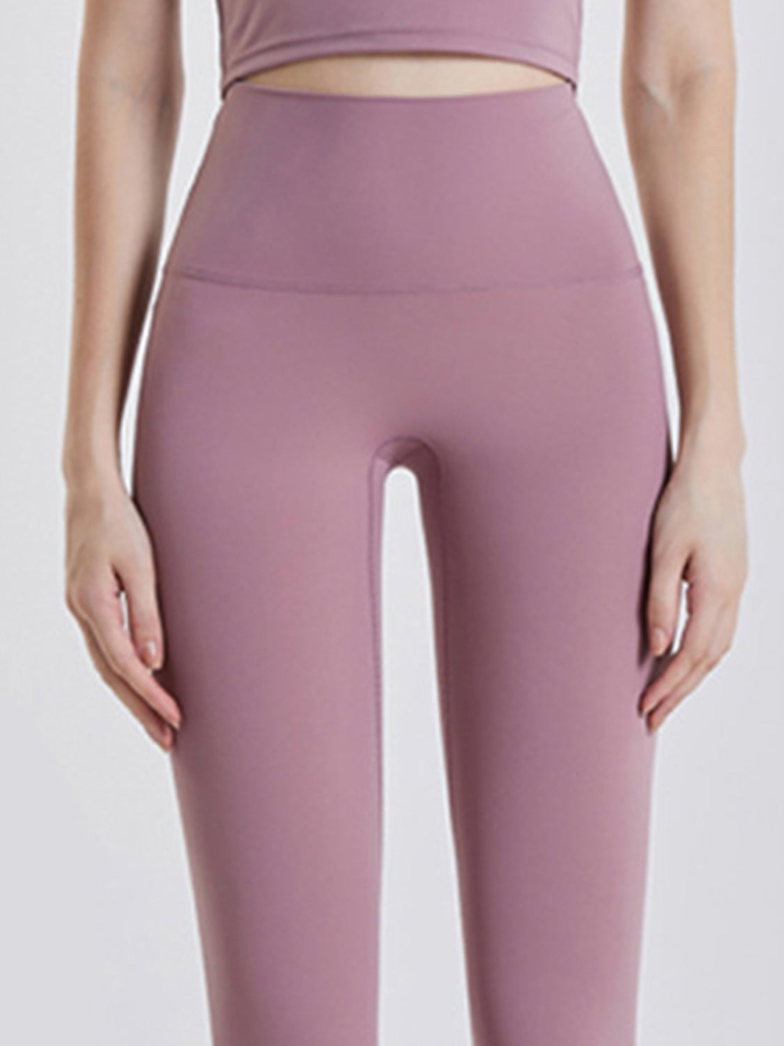 A model stands with hands on her thighs wearing mauve wide-waistband sports leggings with a high-rise fit, smooth construction, and a sleek, close-fitting silhouette.