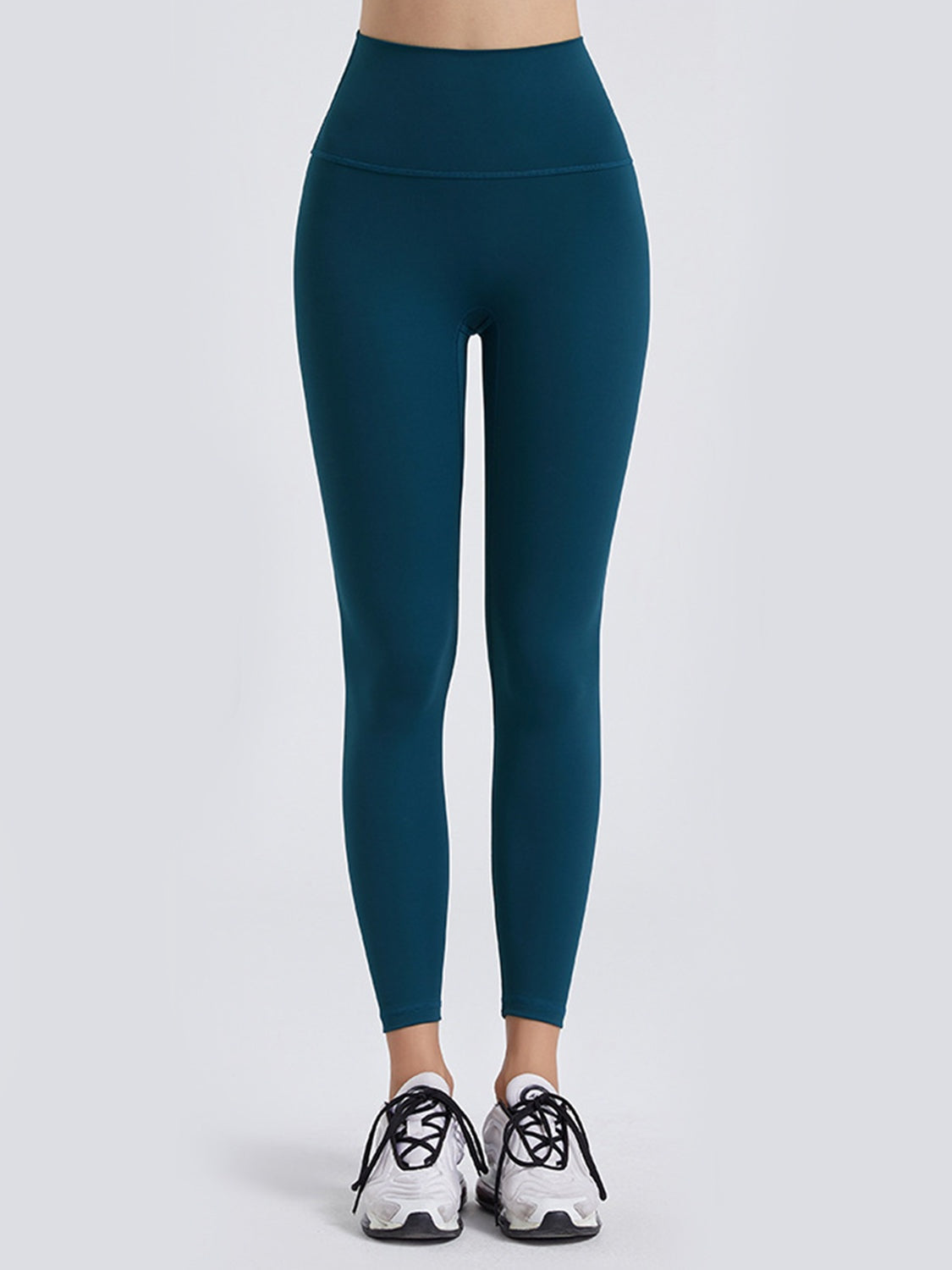 Model wears dark teal wide waistband sports leggings with a high-rise fit, smooth construction, and tapered ankle-length silhouette.