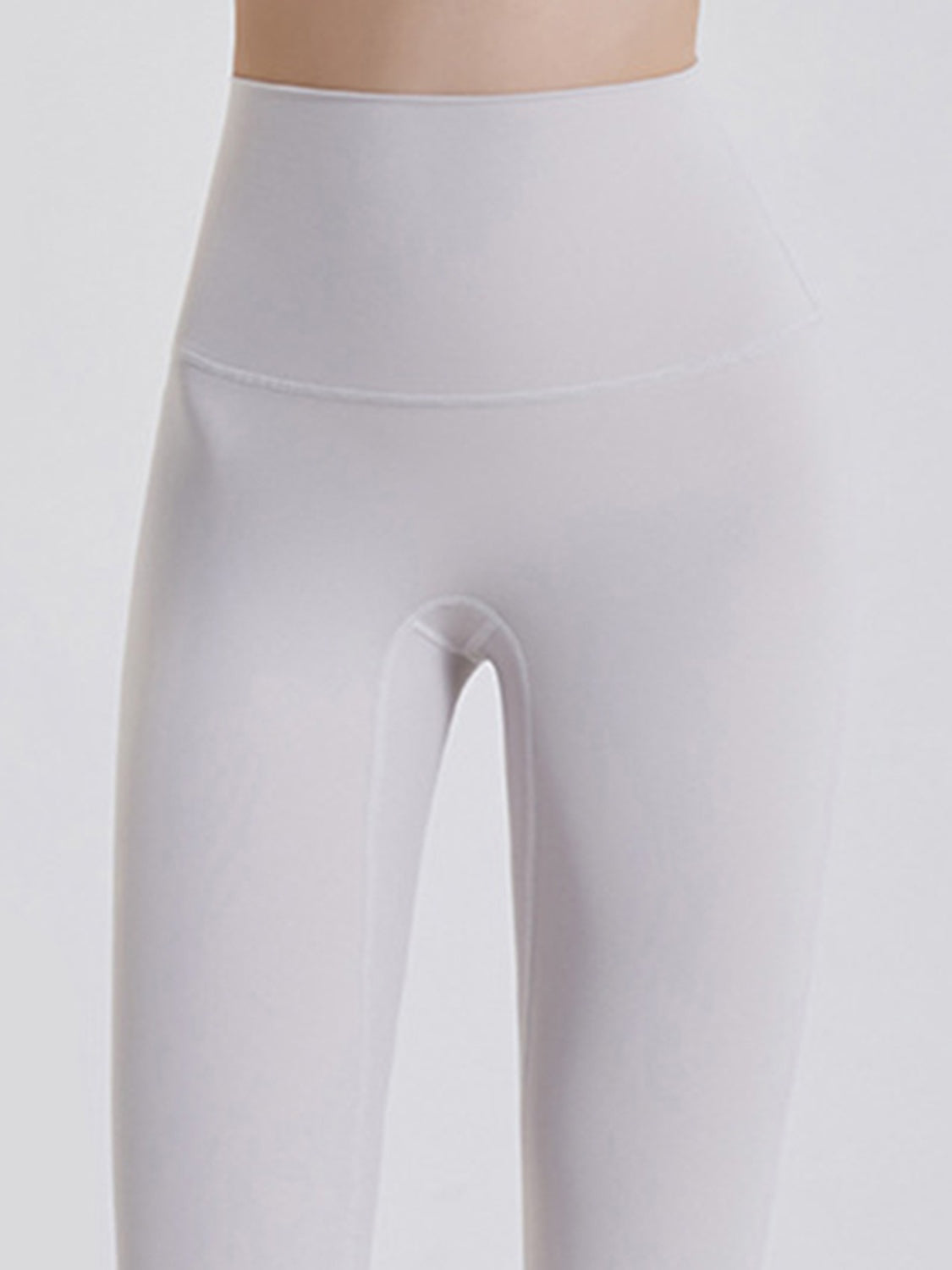 A standing model wears opaque white sports leggings with a wide waistband, smooth stretch fabric, and a close-fitting silhouette through the hips and thighs.