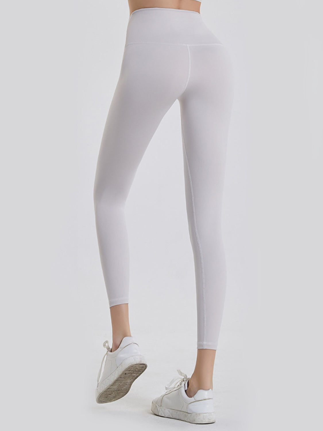 Model shown from behind wearing opaque white wide-waistband sports leggings with a high-rise silhouette, ankle-length legs, and subtle construction seams.