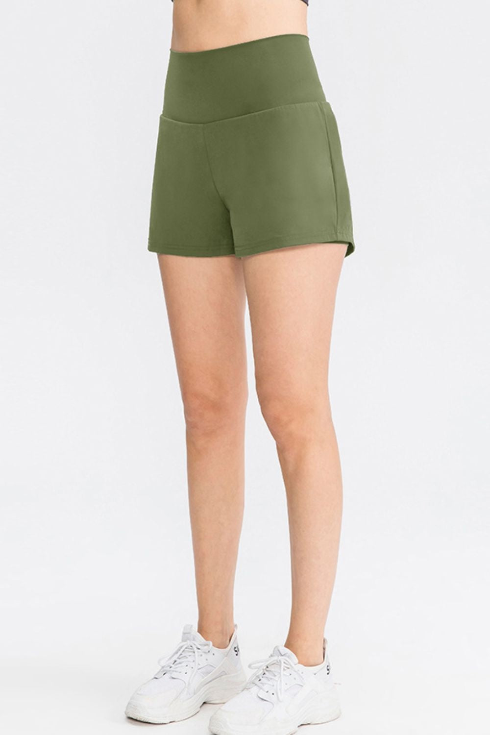 Model wears solid olive green sports shorts with a wide waistband, relaxed short silhouette, and clean stitched construction.