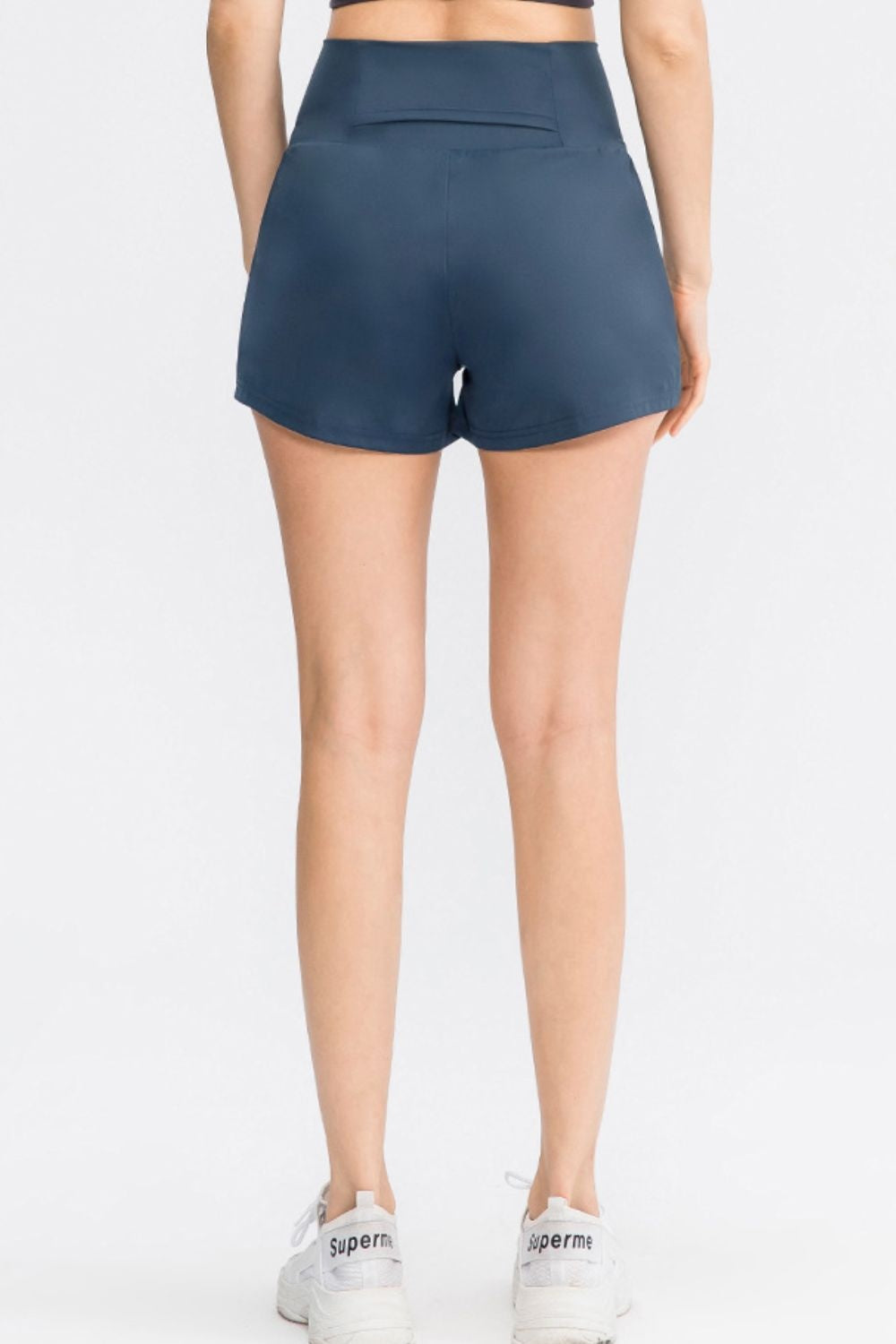A model stands facing away in solid navy sports shorts with a wide waistband, relaxed silhouette, side pockets, and a visible back pocket.