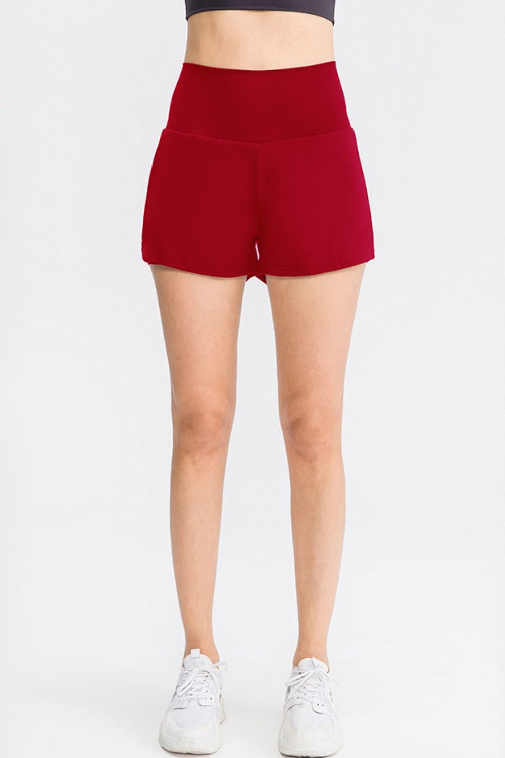 A standing model wears solid red sports shorts with a wide waistband, high-rise fit, smooth construction, and a short relaxed silhouette.