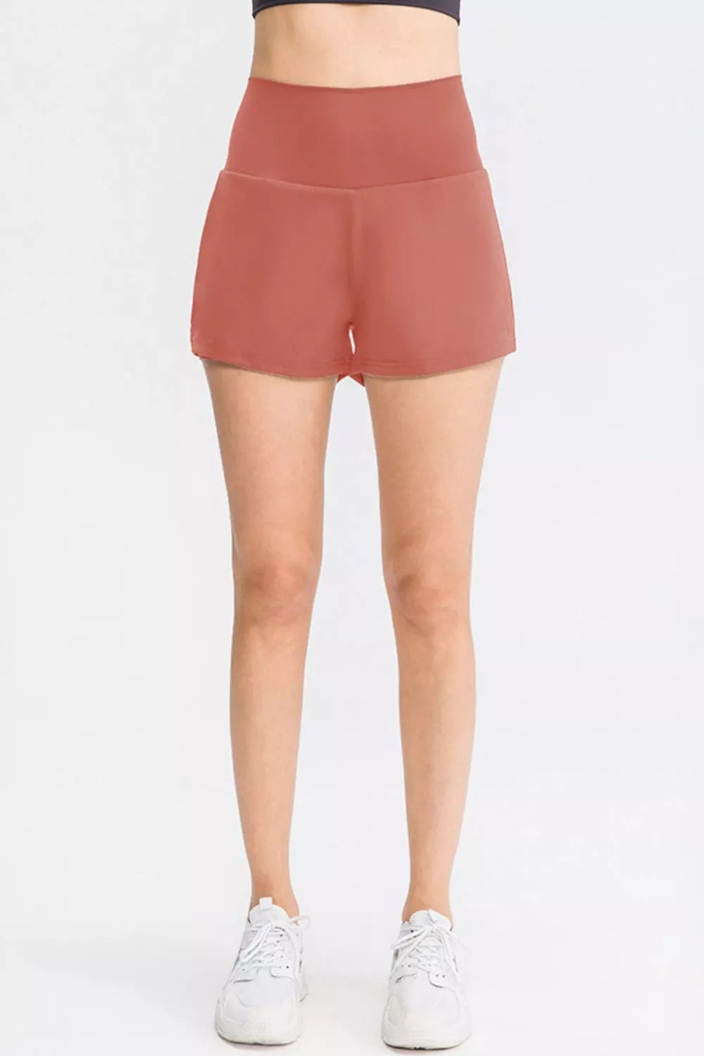 A model stands in solid rust sports shorts with a wide waistband, relaxed silhouette, smooth construction, and practical side pockets.