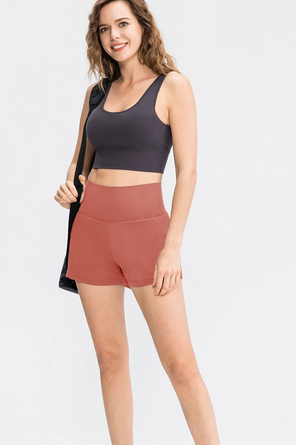 A model stands in solid coral sports shorts with a wide high waistband, fitted silhouette, moderate stretch, and a smooth construction.