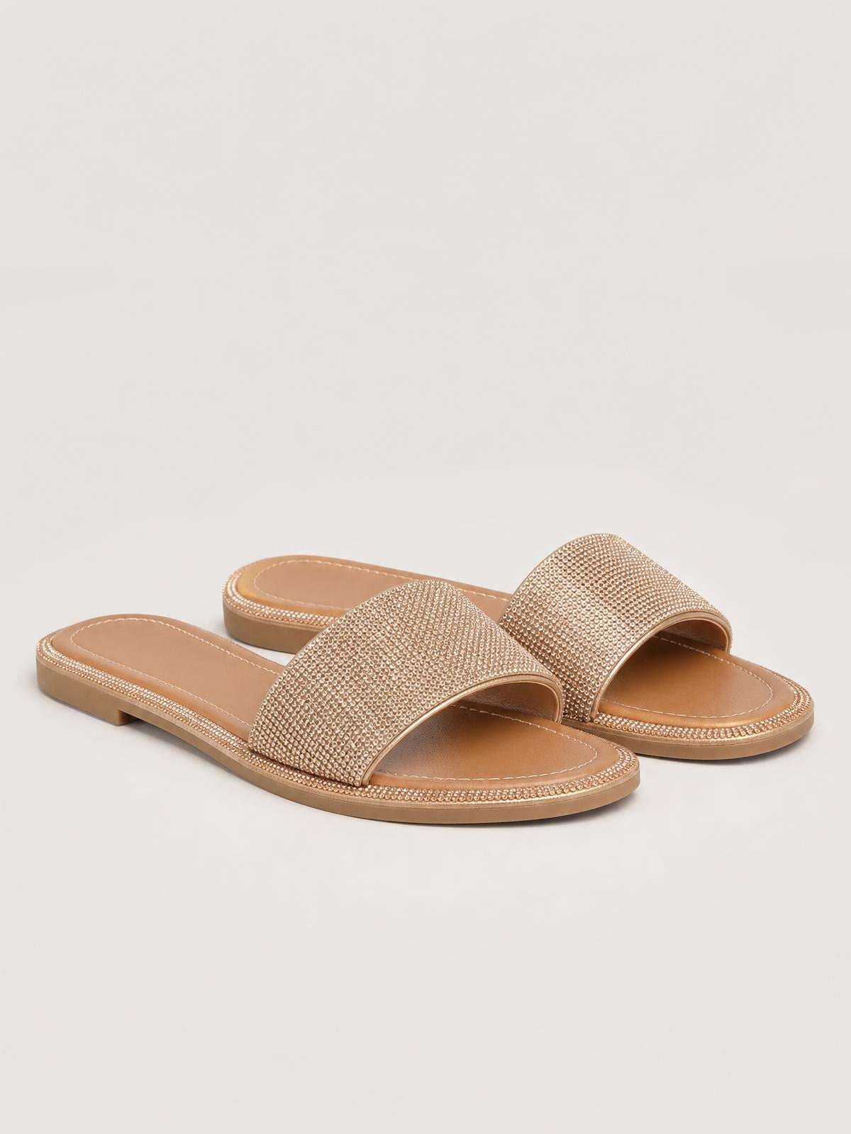 Rose-gold rhinestone open-toe flat sandals feature wide embellished straps, cushioned footbeds, stitched edges, and low flat soles.