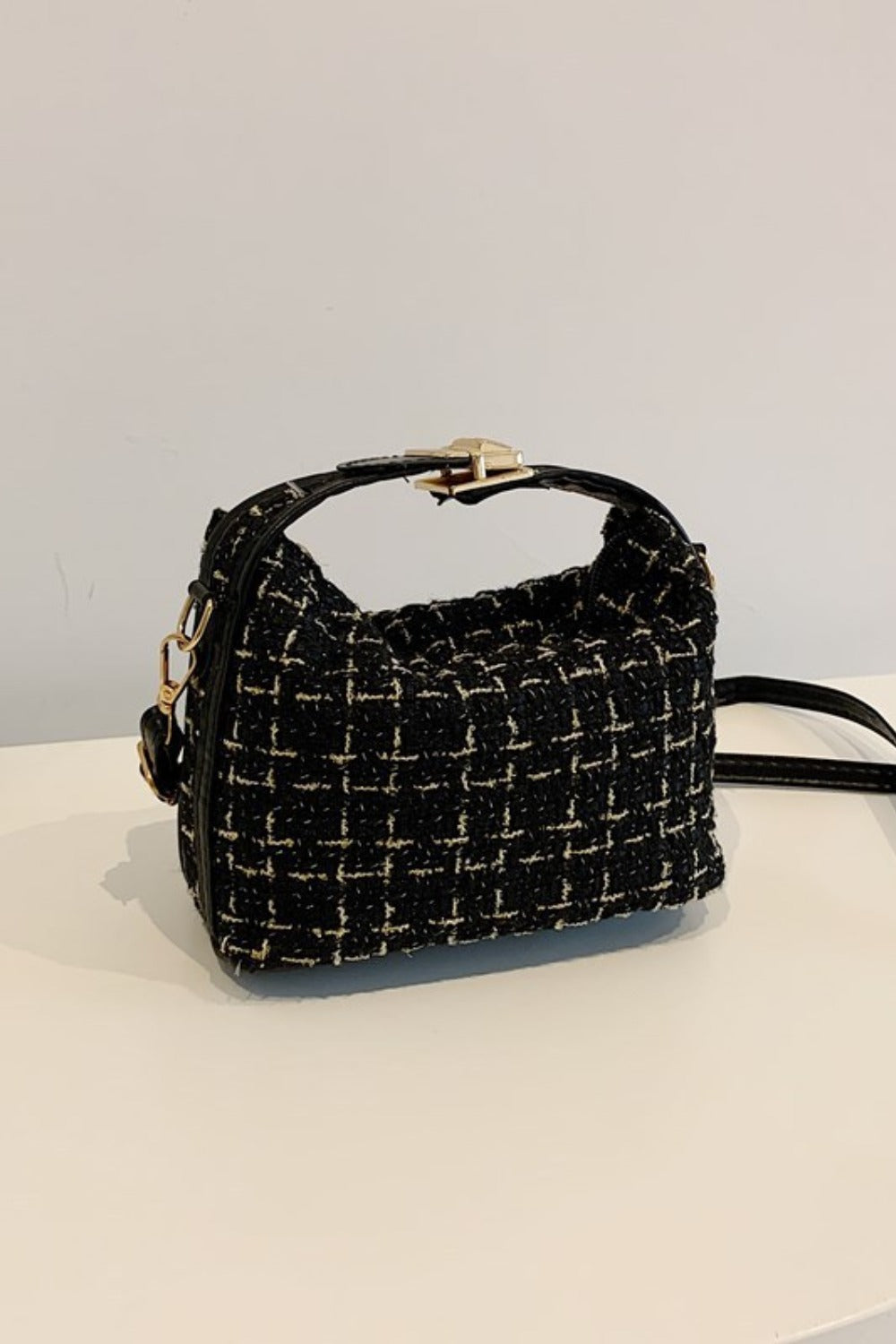 Small black woven shoulder bag with a softly structured rectangular silhouette, short top handle, removable strap, gold-tone hardware, and textured contrast detailing.