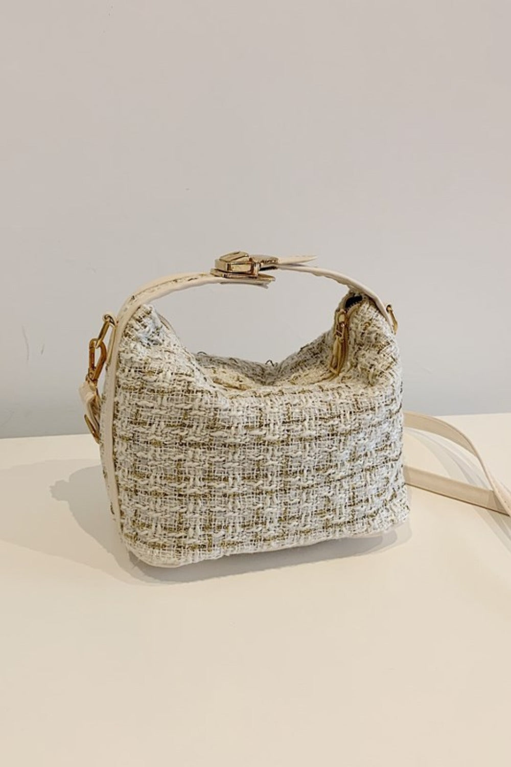 Small cream woven shoulder bag with a softly structured silhouette, short top handle, removable strap, zip-top closure, and sleek gold-tone hardware.