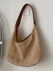 Medium woven straw handbag with a natural beige open-weave body, rounded slouchy silhouette, brown leather trim, and a long shoulder strap.