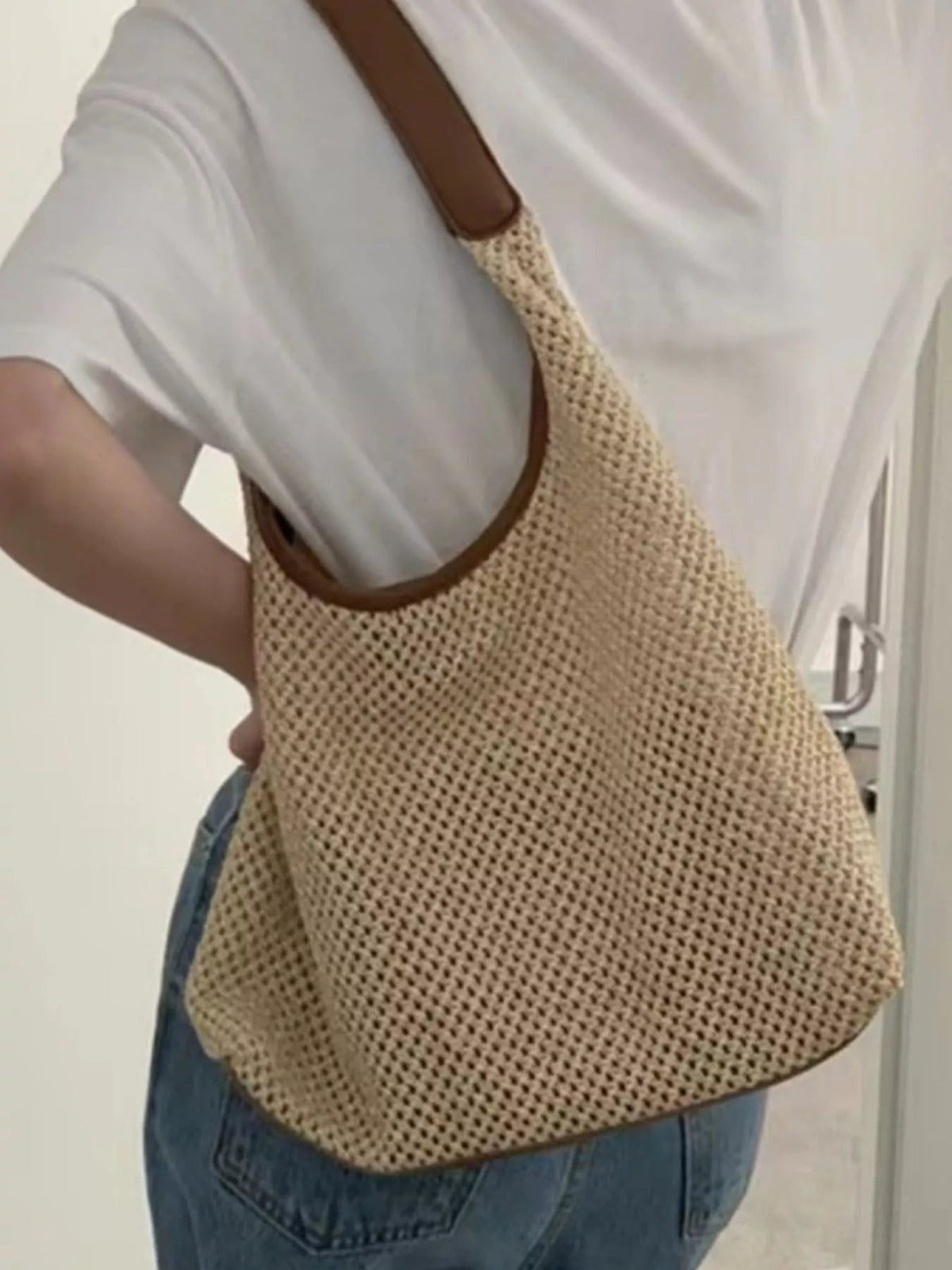 Model wears a medium woven straw handbag with a tan leather shoulder strap, rounded silhouette, and structured construction over a white top.