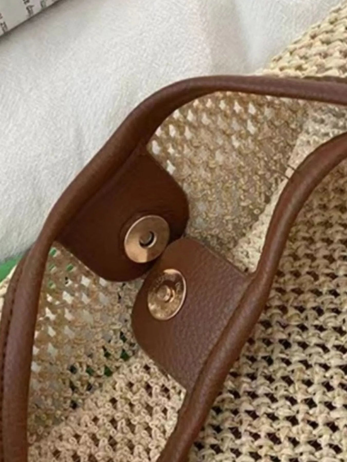 Medium woven straw handbag featuring a natural straw body, brown leather strap, and leather flap secured with round button closures.