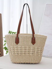 Large woven straw tote bag in a natural beige tone with a structured silhouette, braided texture, and long brown shoulder straps.