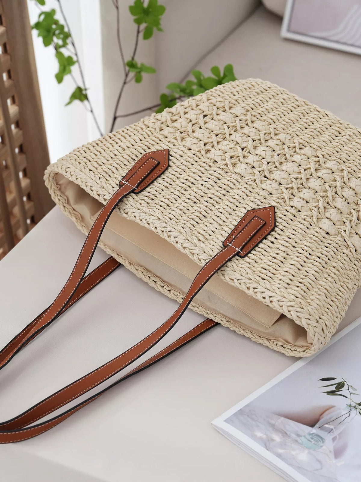 Large woven straw tote bag in natural beige with a structured rectangular silhouette, braided construction, and long brown faux-leather handles with contrast stitching.
