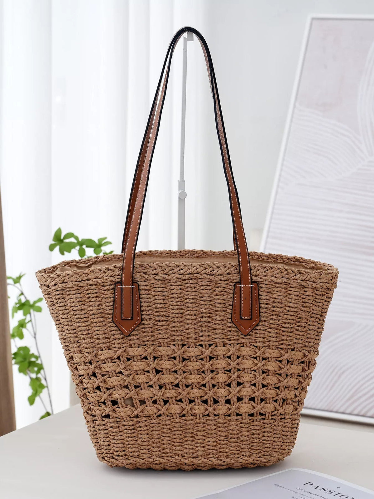 Large tan woven straw tote bag with a spacious open-top silhouette, braided texture, and long brown straps with contrasting white stitching.