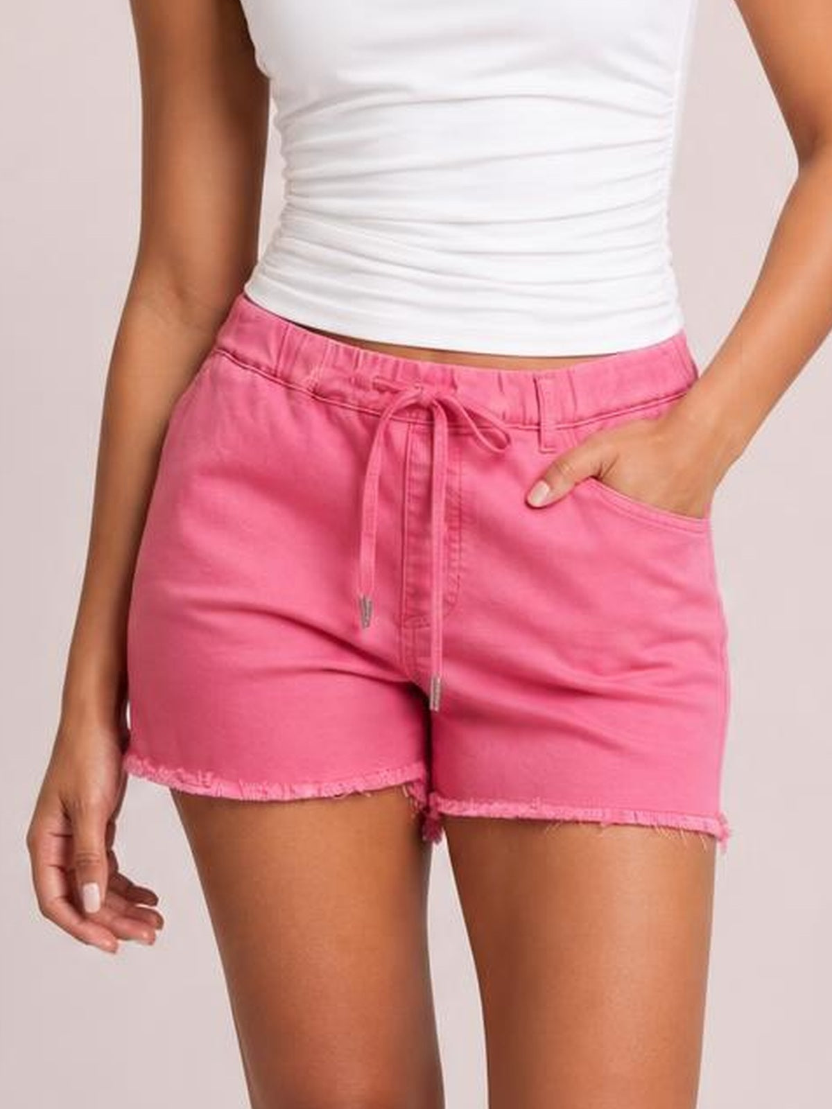 Model wearing bright pink drawstring shorts with an elastic waist, front pockets, relaxed silhouette, and raw hem detailing, one hand tucked into a pocket.