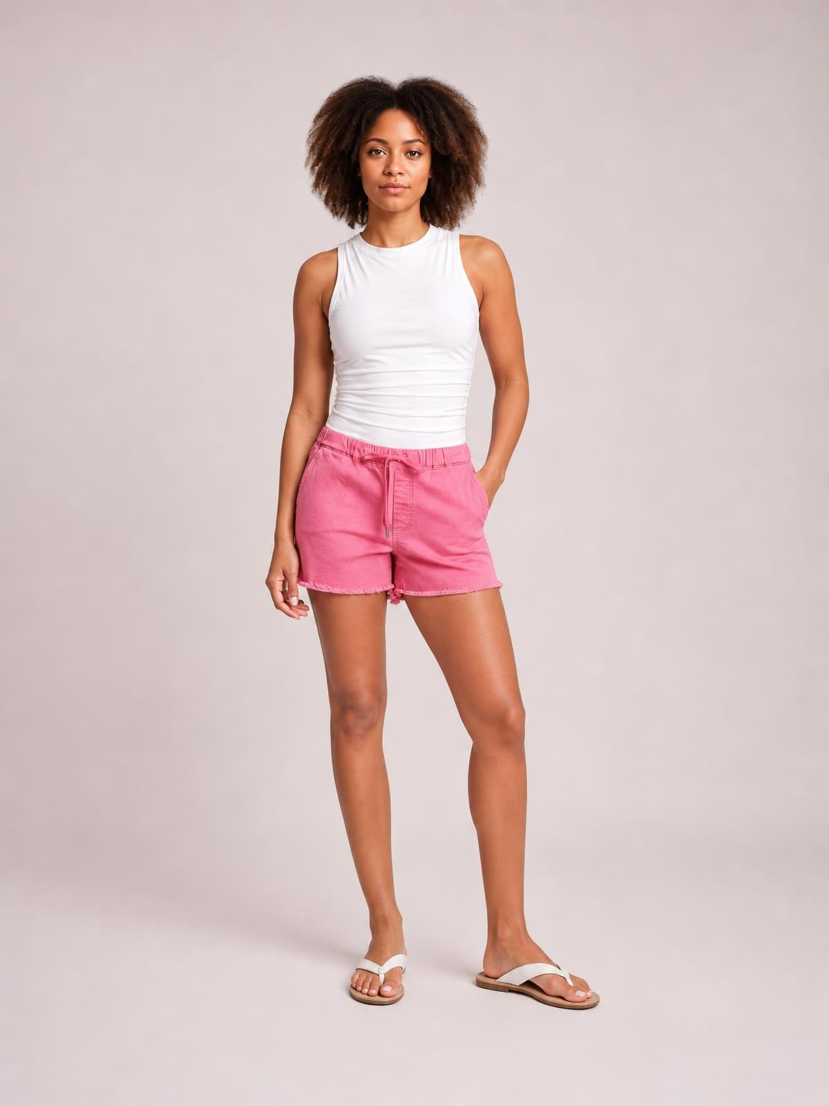 A model stands in pink drawstring raw hem shorts with a relaxed fit, elasticized waist, front pockets, and casually angled legs.