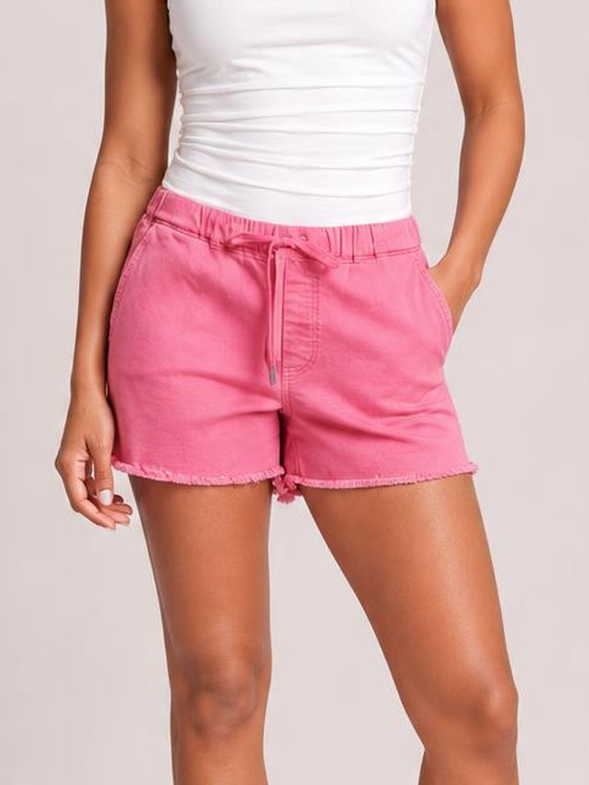 Model wearing pink drawstring raw hem shorts with an elasticized waist, relaxed silhouette, and hands in the pockets.