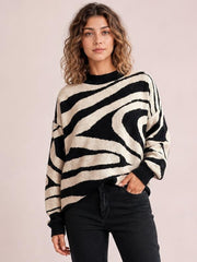 Model wearing an oversized black and cream zebra print round neck sweater with long sleeves, ribbed cuffs and hem, posed with one hand in her pocket.