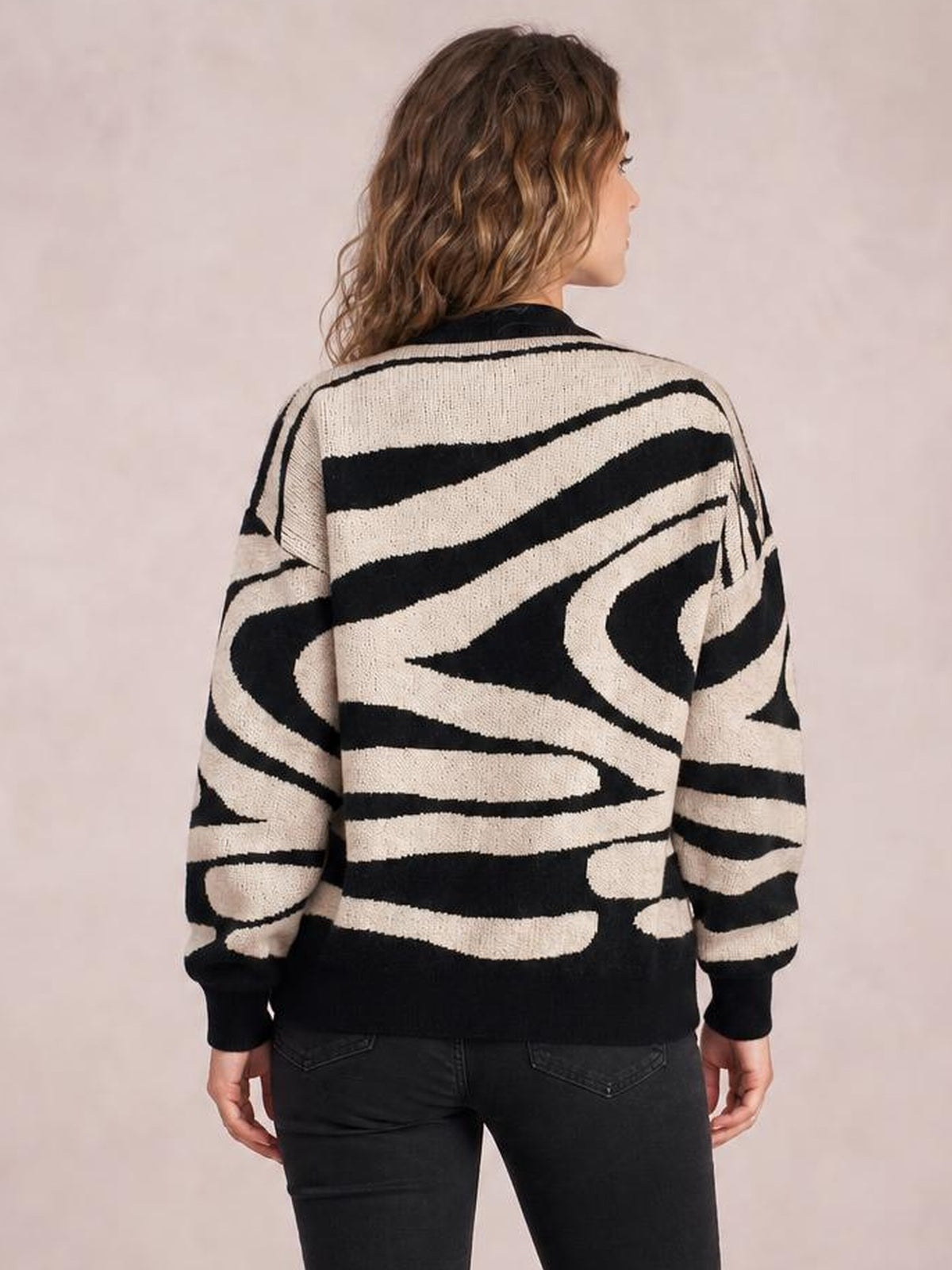 Model shown from the back wearing an oversized zebra print round neck sweater with bold black and cream stripes, long sleeves, ribbed cuffs, and hem.