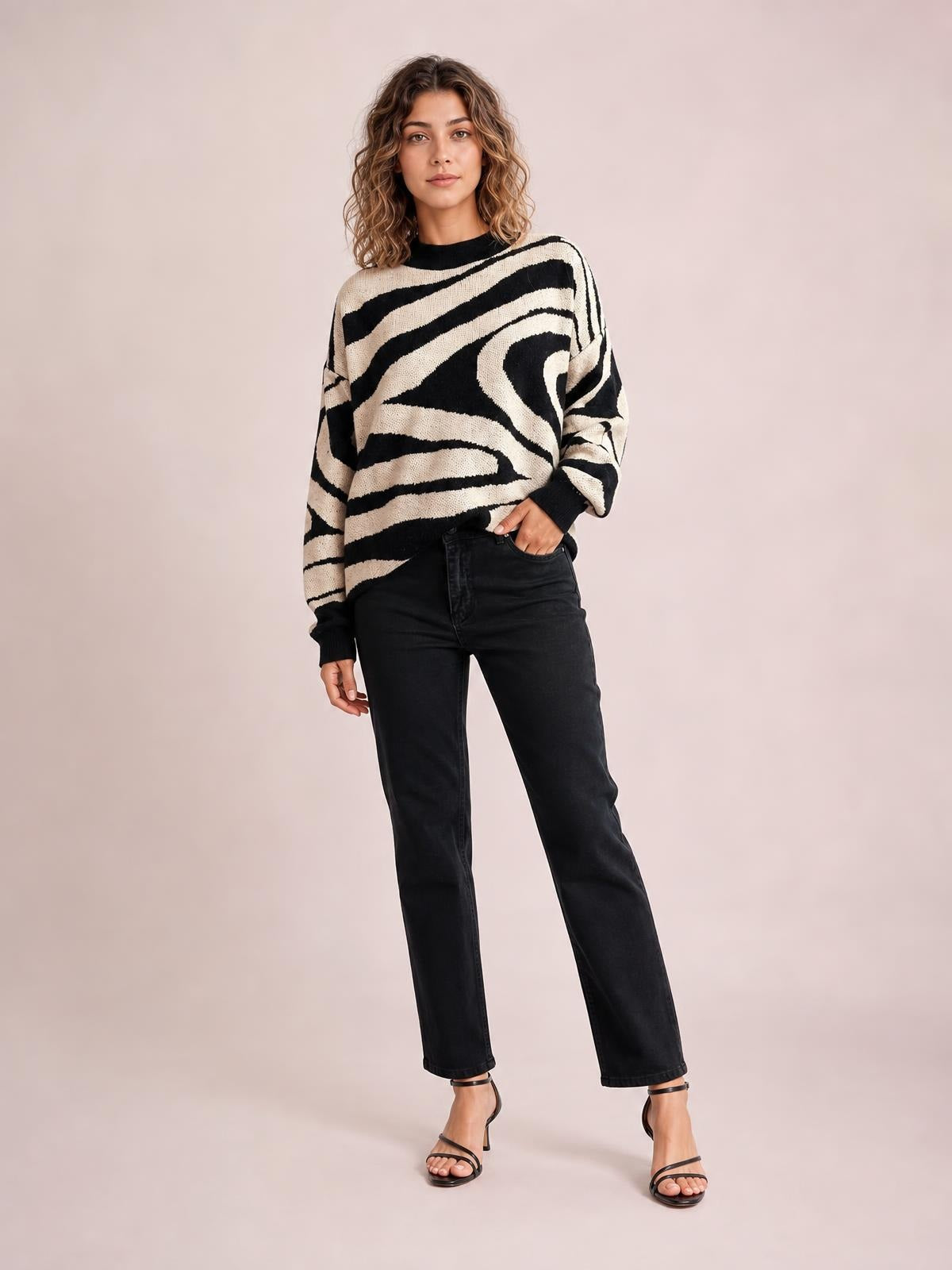 Model wears an oversized black and cream zebra print round neck sweater with dropped shoulders, ribbed cuffs and hem, posing with one hand in her jeans pocket.